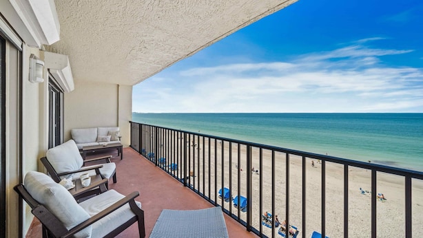 Un balcón con vistas a la playa, mobiliario exterior y barandilla.