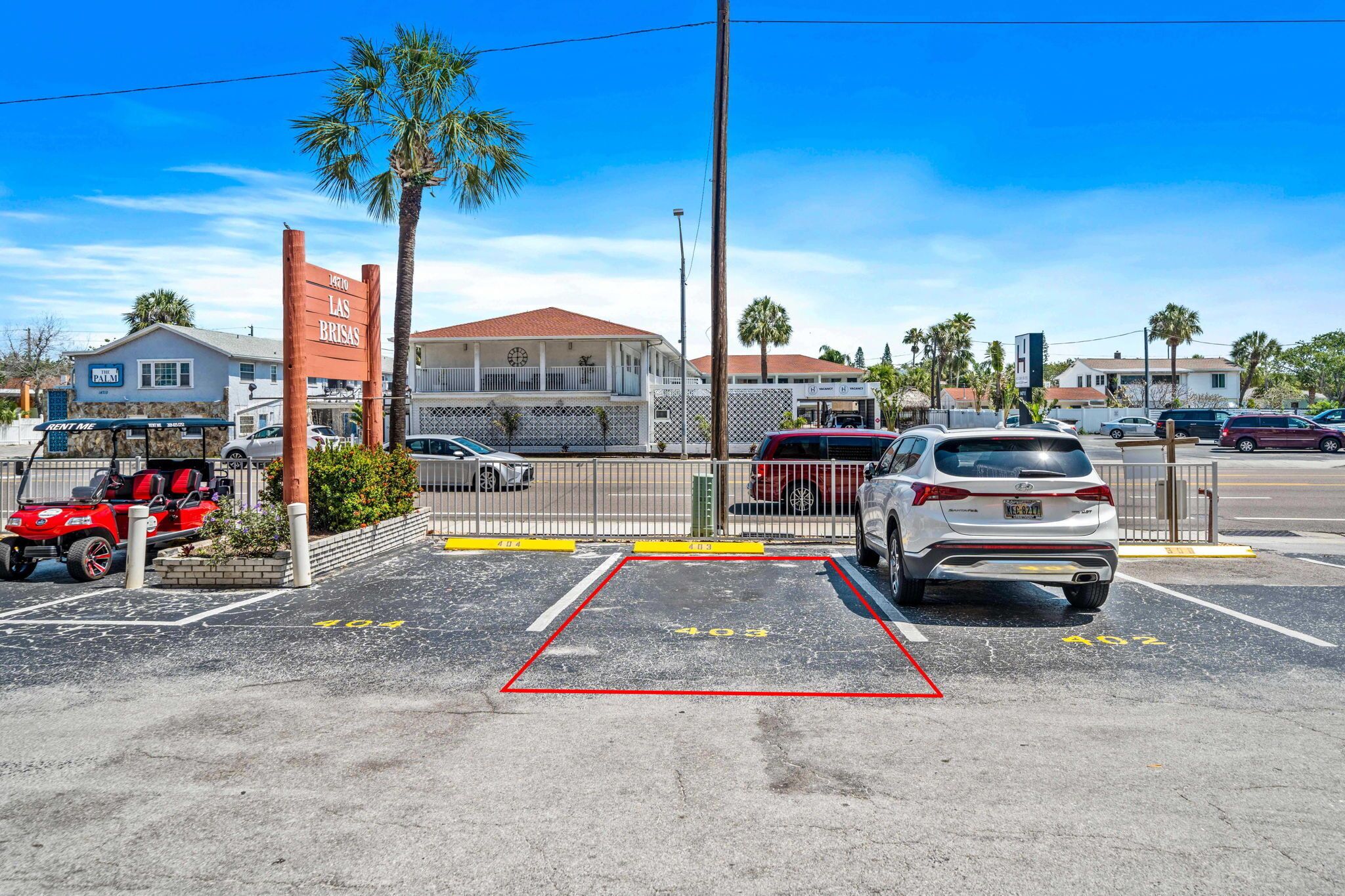 Un parking avec des places réservées aux personnes handicapées, un chariot de golf rouge et un VUS blanc.