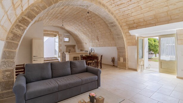 Un vaste espace de vie agrémenté d’une arche en pierre, d’un canapé gris et d’un coin repas avec une table et des chaises.