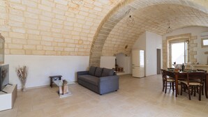 Un vaste espace de vie doté d’un plafond voûté en pierre, d’un canapé gris, d’une table à manger avec des chaises et d’une petite table d’appoint agrémentée d’objets décoratifs.