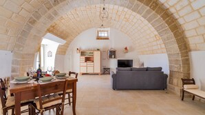 Un plafond en pierre en forme d’arc dans un coin repas, avec une table dressée pour le repas, un canapé et un téléviseur en arrière-plan.
