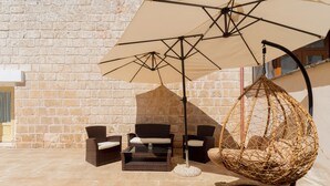 Une terrasse dotée de meubles en osier, d’un fauteuil suspendu et d’un grand parasol.