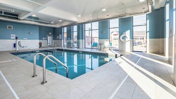 Una piscina interior con señalización de seguridad clara, una silla de salvavidas y vistas al exterior a través de amplias ventanas.