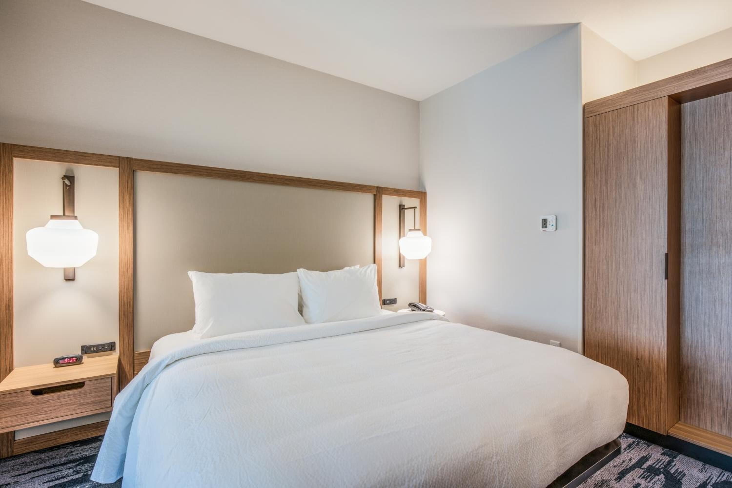 A hotel room with a large bed, wooden headboard, bedside lamps, and a wardrobe.