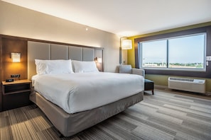 A modern hotel room with a large bed, bedside tables, a nightstand, a chair, a window with a view, and an air conditioning unit. - Holiday Inn Express & Suites Platteville (Platteville)