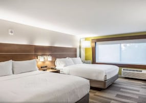 Habitación de hotel con dos camas, una mesita de noche, una lámpara, un ventanal y un equipo de aire acondicionado.