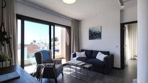 A modern living room with a sofa, a chair, a coffee table, and a large window offering a city view.