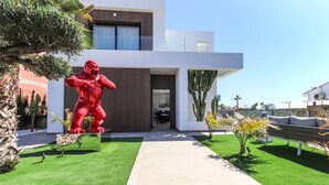 A modern building with a large red sculpture in the foreground, a well-maintained lawn, and a clear sky.