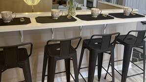 Une cuisine moderne avec un grand îlot central, des tabourets de bar noirs, un lustre et un vase rempli de fleurs.