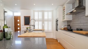Une cuisine moderne dotée d’un plan de travail en granit, d’un revêtement de sol en bois et de meubles blancs.