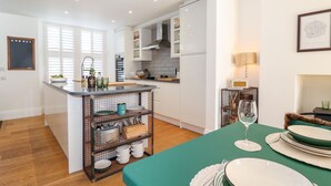 Une cuisine moderne avec des meubles blancs, un îlot central et un coin repas agrémenté d’une nappe verte et d’assiettes.