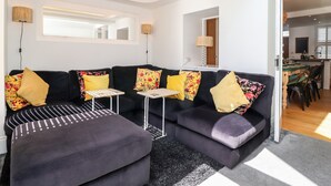 Un salon moderne avec un canapé d’angle noir, deux petites tables d’appoint et un pouf noir.