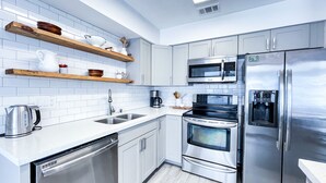 Une cuisine moderne dotée d’appareils électroménagers en acier inoxydable, de meubles blancs et d’étagères en bois.