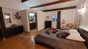 Ein Schlafzimmer mit Bett, Kommode, Fenster und einer Tür zum Badezimmer.