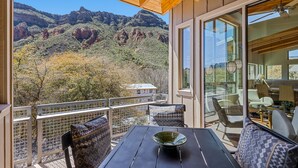 Un balcon avec vue sur les montagnes, une table avec un saladier et des chaises à motifs.
