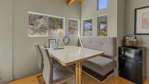 Une cuisine compacte comprenant une table à manger, des chaises, un réfrigérateur et de grandes fenêtres donnant sur l’extérieur.
