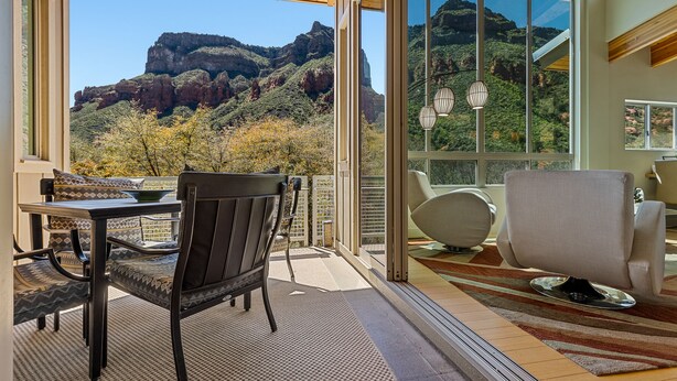 Un balcon avec une table et des chaises, une vue sur un paysage montagneux et une grande fenêtre.