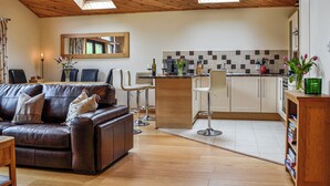 Un espacio habitable amplio con un sofá de cuero, una mesa de comedor y una cocina con armarios blancos y salpicadero de azulejos.