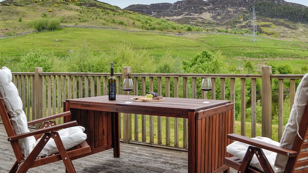 Una terraza de madera con una mesa y sillas, con vistas a un paisaje verde con colinas y una línea eléctrica.