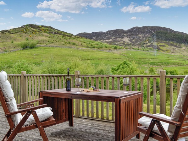 A wooden deck with a table and chairs, overlooking a green landscape with hills and a power line.