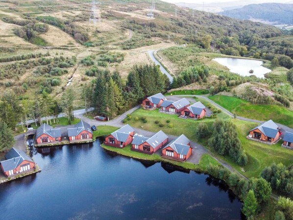 Une propriété au bord du lac, comprenant plusieurs chalets aux toits rouges, un quai et un chemin qui traverse le paysage.