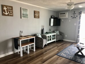 Uma sala de estar com piso de madeira, um armário branco, uma TV fixada na parede e um ventilador de teto.