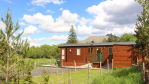 Eine Holzhütte mit einem umzäunten Garten, umgeben von Bäumen und einem Berg im Hintergrund.