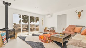 Een moderne woonkamer met een open haard, een bank, een bijzettafeltje en een groot raam met uitzicht op woestijnvegetatie.