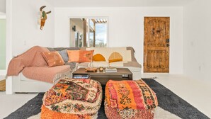 Een moderne woonkamer met een bank, poefjes, een houten deur en een grote spiegel.
