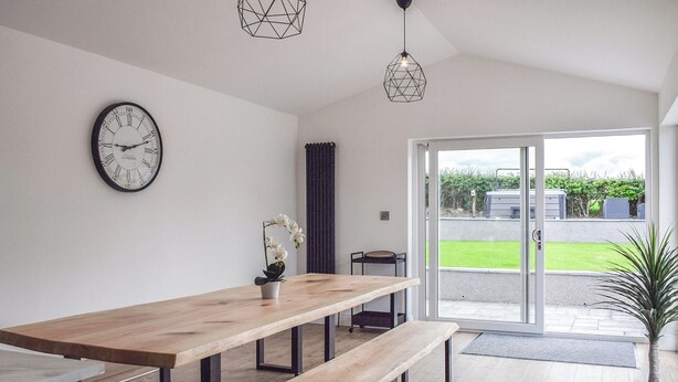 A modern dining area with a wooden table and benches, a wall clock, and a view of the outdoors.