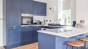 A modern kitchen with blue cabinets, stainless steel appliances, a central island with stools, and a window providing natural light.