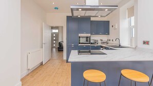 A modern kitchen with dark blue cabinets, a central island with stools, and a view into a living area.