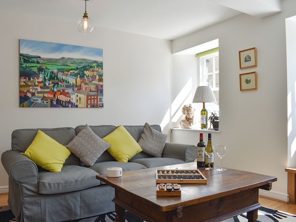 A living room with a grey sofa, a wooden coffee table, a painting, and a bust on a shelf.