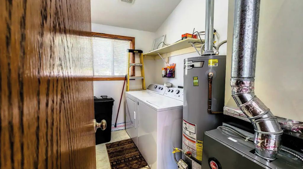 Une petite buanderie comprenant un lave-linge et un sèche-linge, une petite étagère pour ranger les produits de nettoyage et un conduit d’aération.