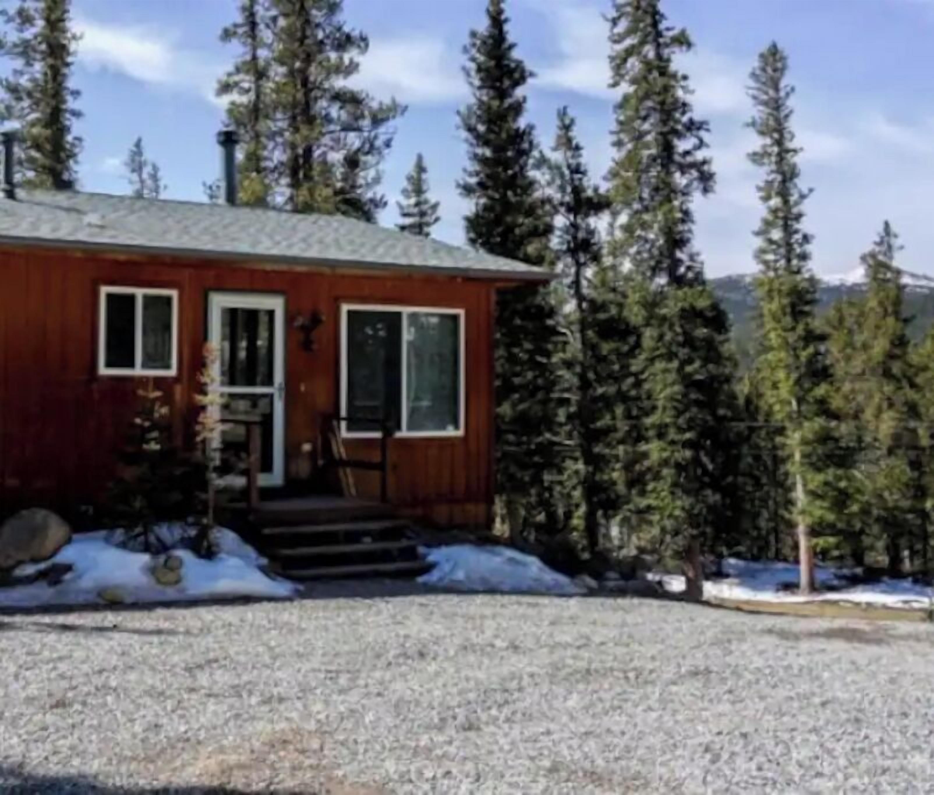 A wooden cabin with a front door, windows, and a gravel driveway.