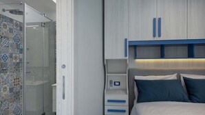 A bedroom with a shower, a bed with blue bedding, and a storage unit with blue handles.