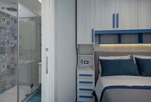 Un dormitorio con ducha, una cama con ropa de cama azul y un mueble de almacenamiento con pomos azules.