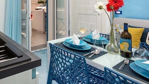 A dining area with a table set for two, featuring blue chairs and plates, a vase with flowers, and a bottle of wine.