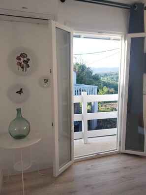 Ein Zimmer mit einer weißen Tür, die auf einen Balkon mit weißer Brüstung führt. Auf einem kleinen Tisch steht eine Glasvase.