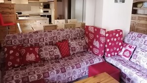 Een gezellige woonkamer met een gestreept bankje, een houten salontafel en een keuken op de achtergrond.