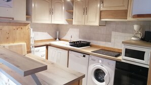 Een kleine keuken met houten kastjes, een inbouwvaatwasser, een wasmachine en een magnetron.