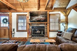 Cozy living room with a stone fireplace, comfortable seating, and large window.