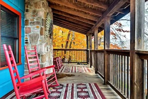 Relax on the porch with a view of autumn foliage, surrounded by a stone wall and a wooden railing.
