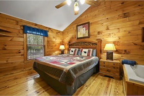 Cozy bedroom with a large bed, wooden nightstand, and bench, featuring a wooden headboard and framed artwork.
