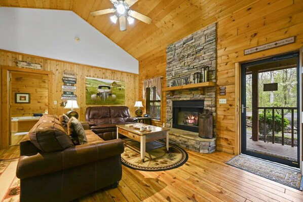 Cozy living room with a fireplace, leather sofa, and coffee table, featuring a stone accent wall and a welcoming atmosphere.