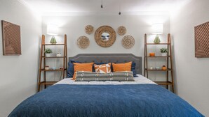 Camera da letto con un letto, una testiera, una ventola a soffitto e decorazioni alle pareti, tra cui mensole con piante e oggetti decorativi.