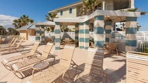Un resort con zona de piscina que incluye tumbonas y sombrillas, un área de estar cubierta y un edificio con balcón.