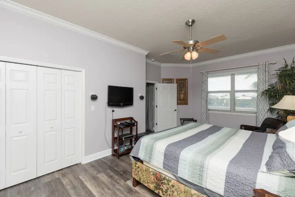 A bedroom with a bed, a ceiling fan, a TV, and a window with curtains.
