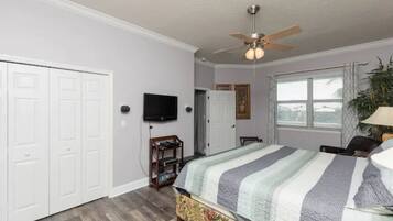A bedroom with a bed, a ceiling fan, a TV, and a window with curtains.