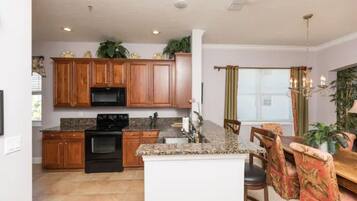 A kitchen with wooden cabinets, a black stove, granite countertops, and a dining area with a table and chairs.